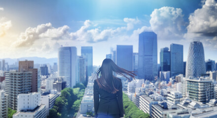 日本の街・都市・朝日を受けたオフィスビル群を前に佇み風を受けて髪をなびかせる会社員の女性の出勤　就職・ビジネス・はじまり・決意・目標・挑戦のイメージ