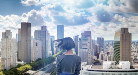 日本の街・都市・朝日を受けたオフィスビル群を前に佇み風を受けて髪をなびかせる会社員の女性の出勤　就職・ビジネス・はじまり・決意・目標・挑戦のイメージ