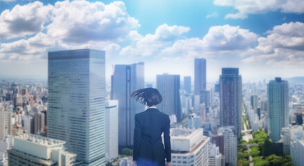 日本の街・都市・朝日を受けたオフィスビル群を前に佇み風を受けて髪をなびかせる会社員の女性の出勤　就職・ビジネス・はじまり・決意・目標・挑戦のイメージ