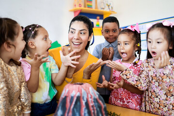 Teacher and group of children learning about volcanos at science kindergarten project. Multiracial kids studying at elementary school. Education concept