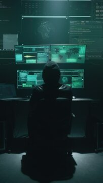 Minimalistic concept shot of alone hacker programmer surrounded by programming codes interface in a dark ambient cyber space, sitting at a table with four monitors doing a hacking attack. Vertical