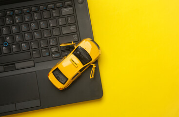 Laptop with taxi car miniature on yellow background