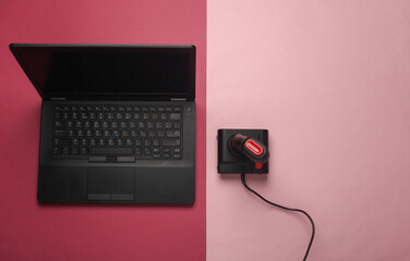 Laptop with retro joystick on pink background