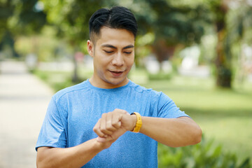 Young man in a blue shirt checking his smartwatch while outdoors in a park setting