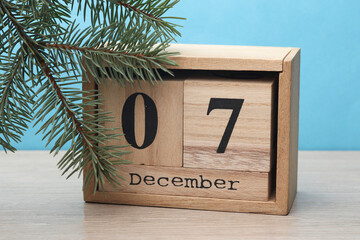 Wooden block calendar with date December 07 and pine tree on table and blue background