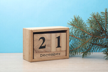 Wooden block calendar with date December 21 and pine tree on table and blue background