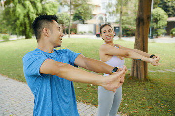 Man and woman in athletic wear warming up together by stretching their arms during an outdoor exercise in the park