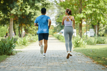 Man and woman jogging together along a park path during a sunny day, both wearing athletic wear