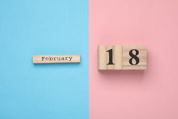 Wooden block calendar with date February 18 on pink blue pastel backround. Top view. Flat lay