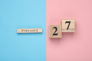 Wooden block calendar with date February 27 on pink blue pastel backround. Top view. Flat lay