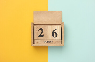 Wooden block calendar with date March 26 on blue yellow backround. Top view. Flat lay