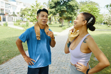 Man and woman in athletic wear relaxing and talking after an outdoor exercise routine in a park