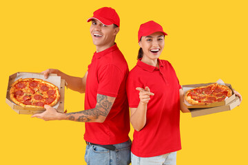 Young couriers with tasty pepperoni pizza on yellow background