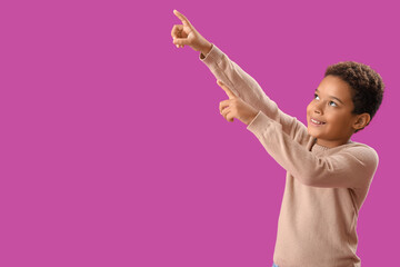 Little African-American boy pointing at something on purple background