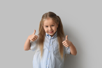 Happy little girl showing thumbs-up on grey background
