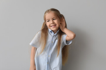 Happy little girl with hearing problem on grey background