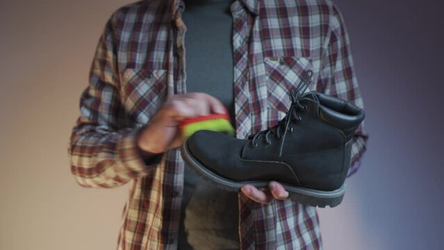 Man cleaning black boots with brushes in the studio. Male brushing nubuck footwear with a small scrub brush. Theme of care for winter shoes. Washes dirty black fall booties, workshop shoes cleaner. 