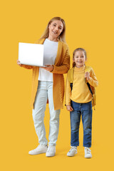 Fototapeta premium Little schoolgirl and her grandmother with laptop on yellow background