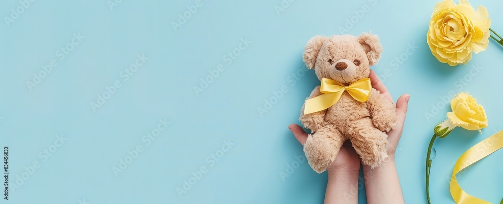 Wall mural Photo of a person holding a teddy bear with a yellow ribbon around its lowered head, on a light blue background. Web banner with a wide angle view. - Wall murals