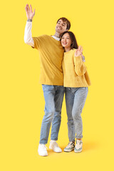 Stylish young couple waving hands on yellow background
