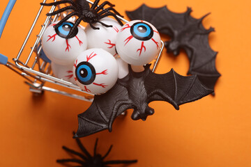 Minimalistic Halloween layout with eyeballs, bats and spiders in a shopping cart on orange...