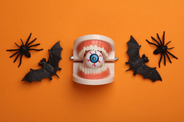 Minimalistic Halloween layout with eyeball in jaw, bats and spiders on orange background