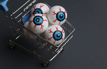 Minimalistic Halloween layout with eyeballs in a shopping cart on dark gray background