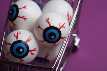 Minimalistic Halloween layout with eyeballs in a shopping cart on purple background