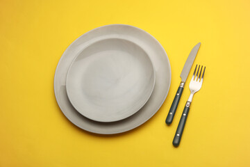 Plates with cutlery on yellow background. Table setting. Top view