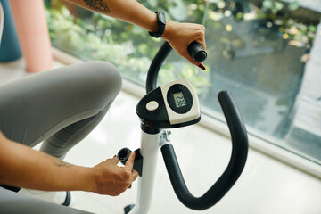 Close-up shot of a woman adjusting the settings on an exercise bike, focusing on the hands and...