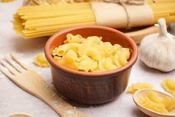 Bowl with uncooked pasta on light background, closeup