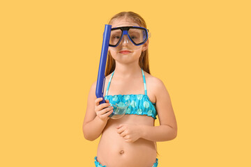 Cute little girl in swimsuit with snorkeling mask on yellow background