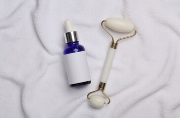 Jade facial roller with serum bottle on white towel. Beauty concept. Top view