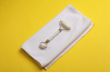 Jade facial roller with towel on yellow background. Beauty concept