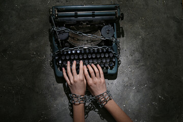 Female hands with vintage typewriter and chains on grey grunge background. Printing ban concept