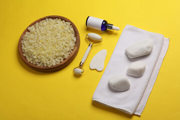 Jade facial roller and gua sha scraper, serum bottle, sea salt, towel on yellow background. Top...