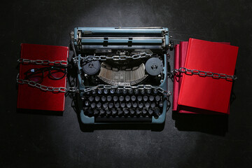 Vintage typewriter with chains, books and eyeglasses on black background. Printing ban concept