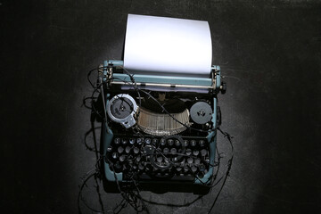 Vintage typewriter with paper sheet, barbed wire and handcuffs on black background. Printing ban...
