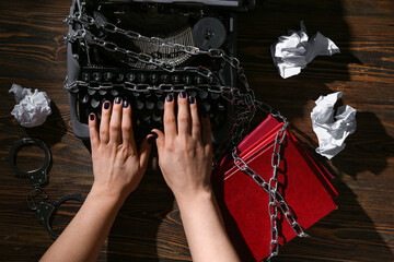 Female hands with vintage typewriter, books and chains on wooden background. Printing ban concept