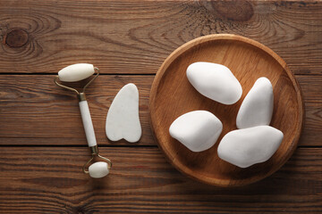 Jade facial roller and gua sha scraper, pebbles on wooden background. Beauty concept.