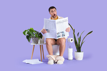 Shocked young man reading newspaper on toilet bowl against lilac background