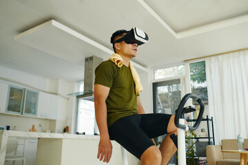 A man sitting on a stationary bike, resting after a virtual reality exercise session in a spacious,...