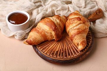 Wooden board with tasty croissants and bowl with jam on brown background