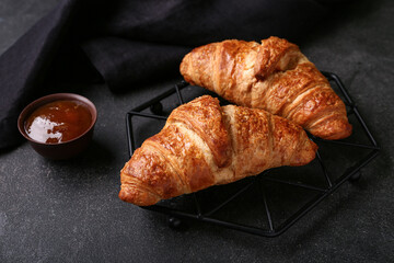 Stand with tasty croissants and bowl of jam on black background