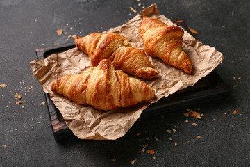 Board with tasty croissants on black background