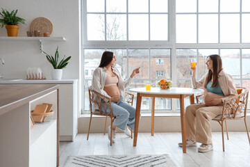 Pregnant female friends drinking juice at table in kitchen