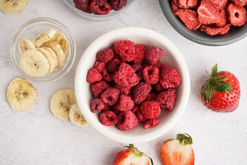 Bowls with freeze-dried raspberries and bananas on white background