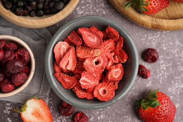 Bowl with freeze-dried strawberry and cherries on grey background