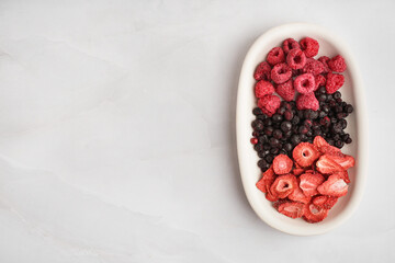Bowl with tasty freeze-dried raspberries, strawberries and blueberries on white background