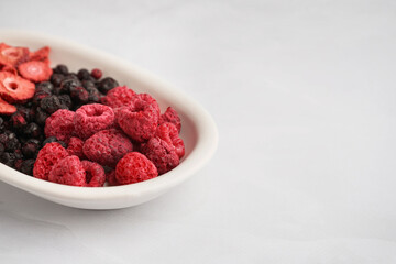 Bowl with tasty freeze-dried raspberries, strawberries and blueberries on white background